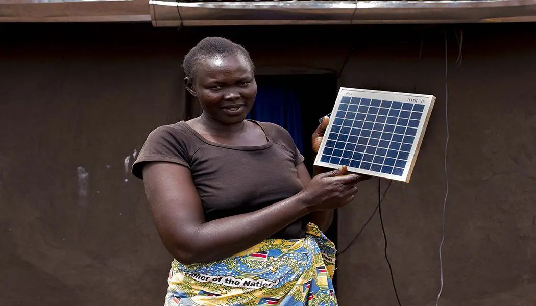 Homeowner beside a rooftop solar installation in Kiryandongo
